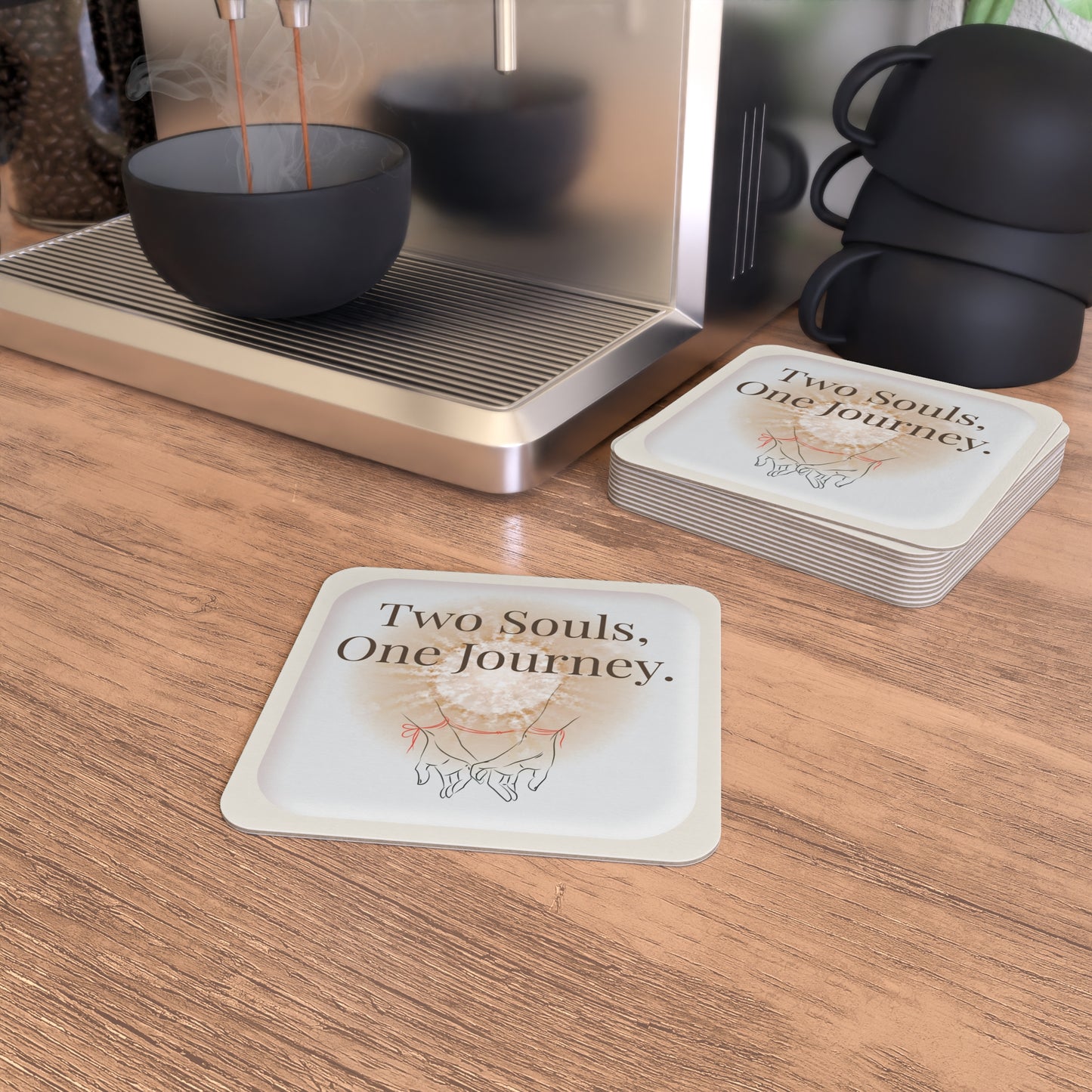 Coasters with 'Two Souls, One Journey' text on a wooden surface with a coffee machine.