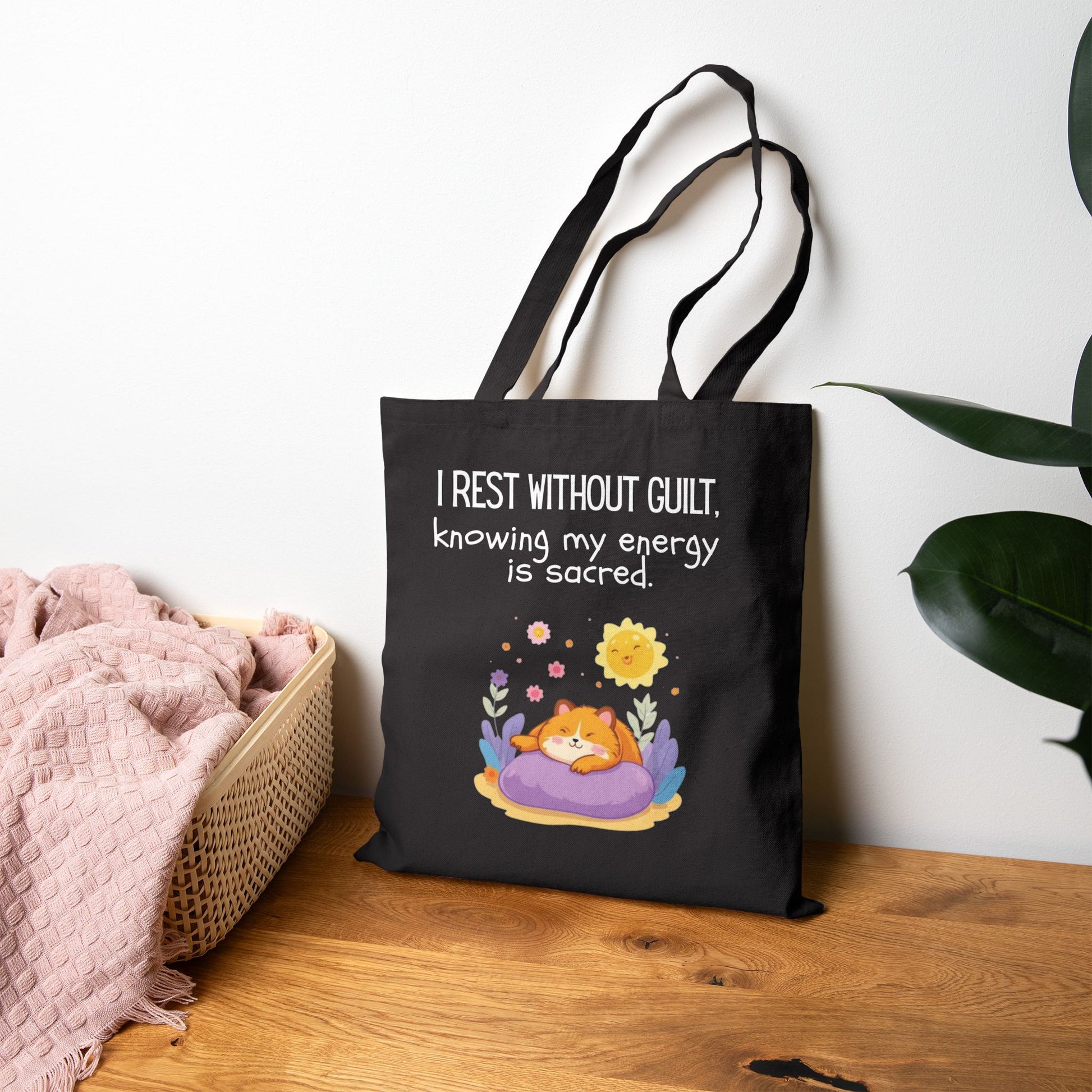Black tote bag with a motivational quote and cartoon design on a wooden surface.