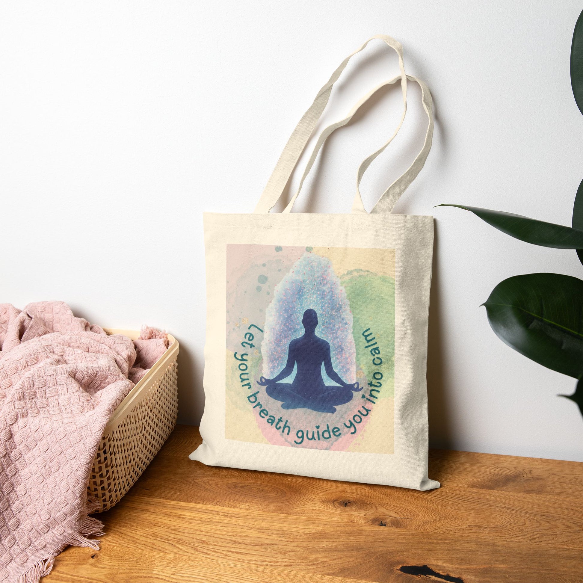 Tote bag with a meditation design and text on a wooden surface with a plant in the background