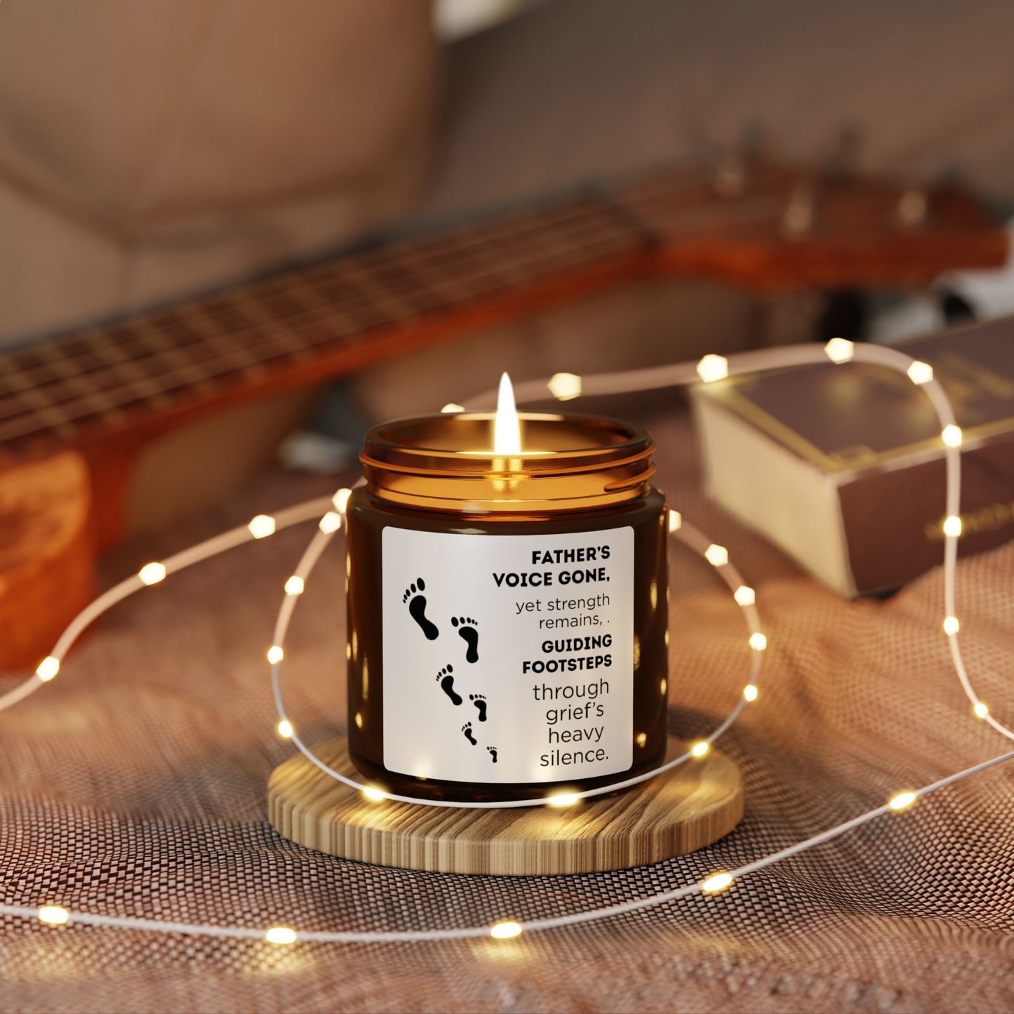 Candle with a message on a wooden coaster surrounded by string lights, with a guitar in the background.