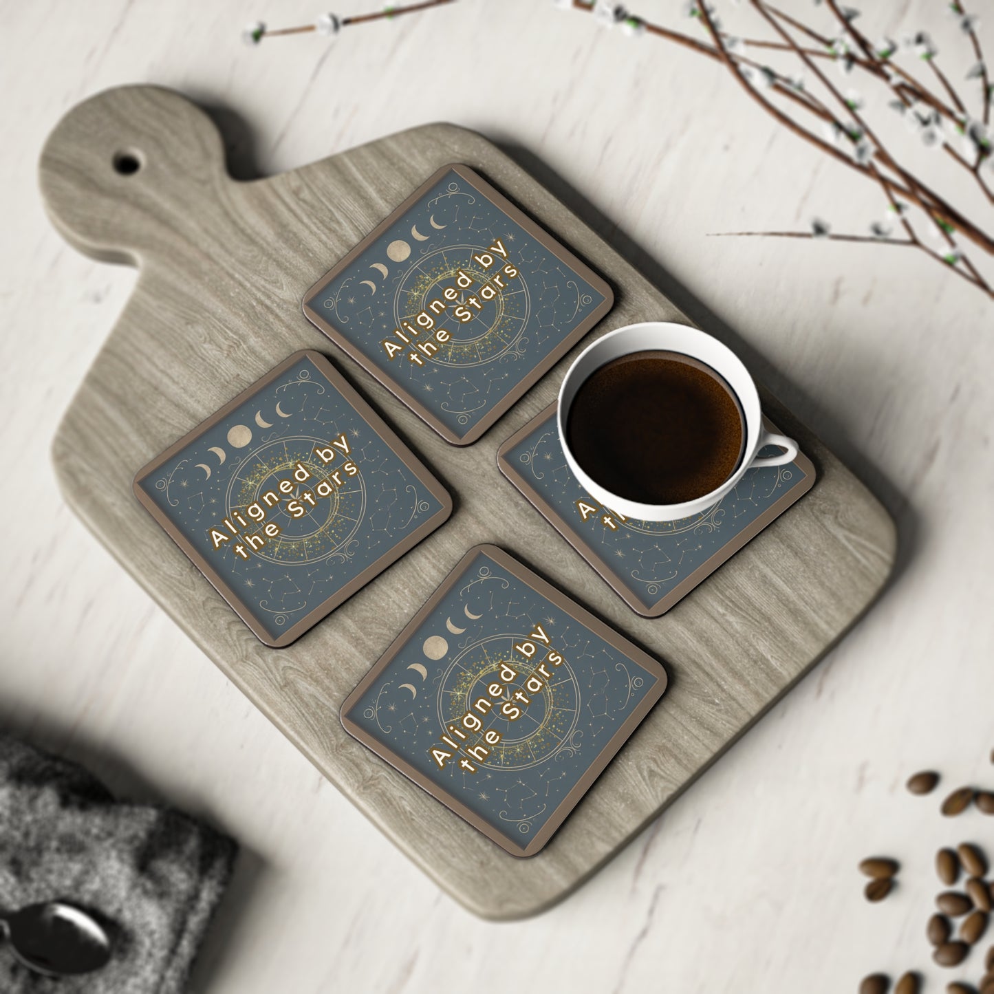 Set of four coasters with moon phases and 'Aligned by the Stars' text on a wooden tray with a cup of coffee.